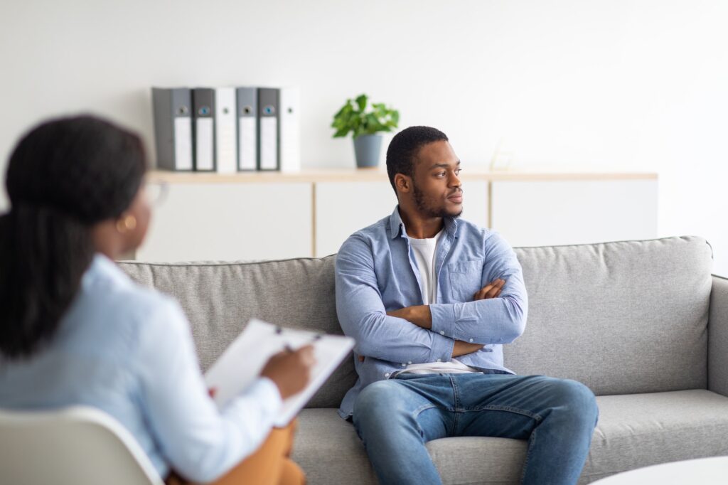 Young psychologist working with emotionally detached black male patient at clinic, trying to help